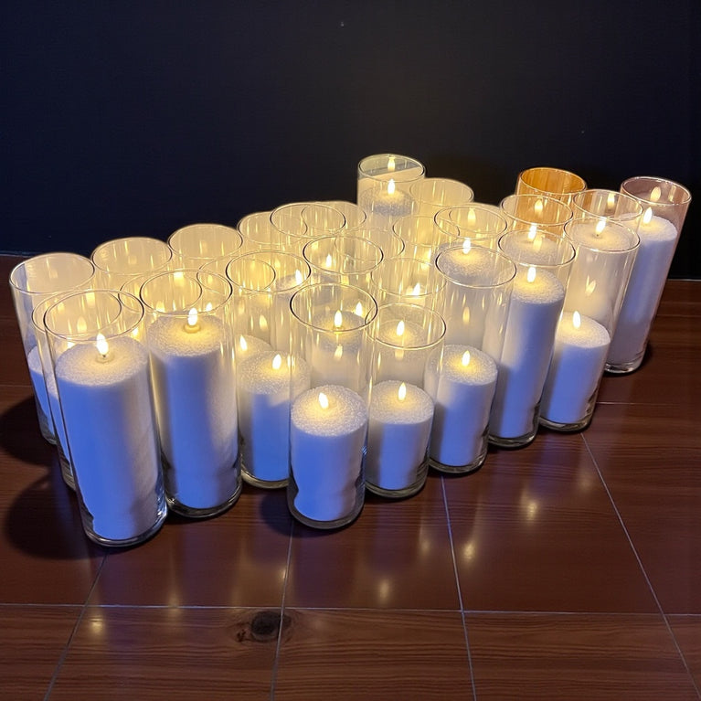 Multiple white candles in glass holders arranged on a wooden surface.