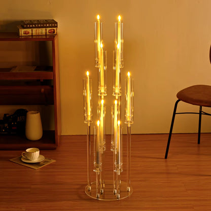 Clear glass candle holder with multiple candles on a wooden floor, with a bookshelf and chair in the background.