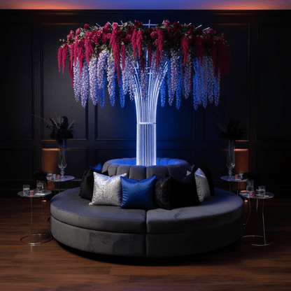 Modern circular sofa with decorative pillows under a floral wedding prop rental in a dimly lit room.