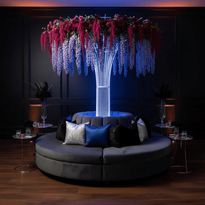 Modern circular sofa with decorative pillows under a floral wedding prop rental in a dimly lit room.