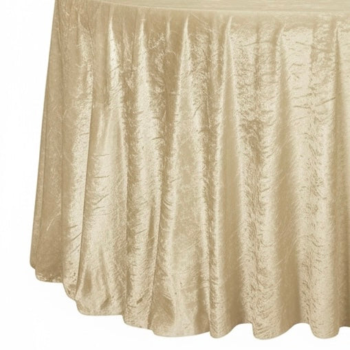 Round table draped with a textured champagne velvet tablecloth on a white background