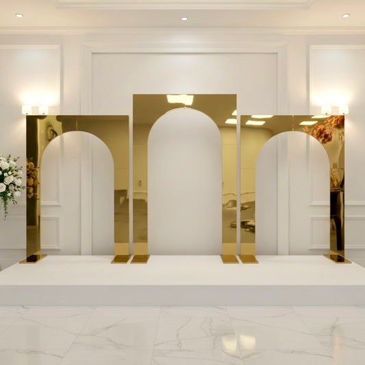 Gold arch-shaped mirror wedding backdrops on a white platform with a white wall and lights in the background