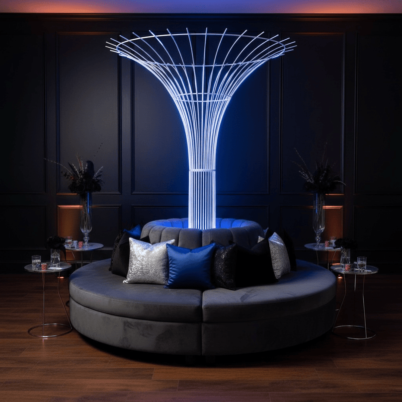 Modern circular sofa with decorative pillows in a dimly lit room with a futuristic party rental light sculpture.
