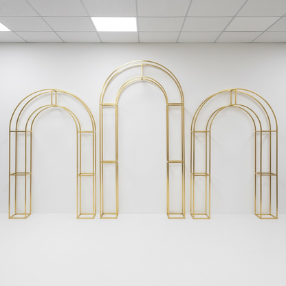 Set of three gold arch-shaped metal wedding backdrop frames on a white wall.