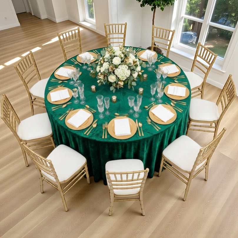 Round table set for a wedding event with emerald green tablecloth, gold plates, and chairs.