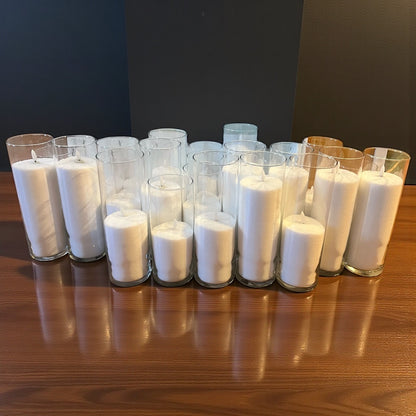 Row of white candles in clear glass holders on a wooden surface with a dark background