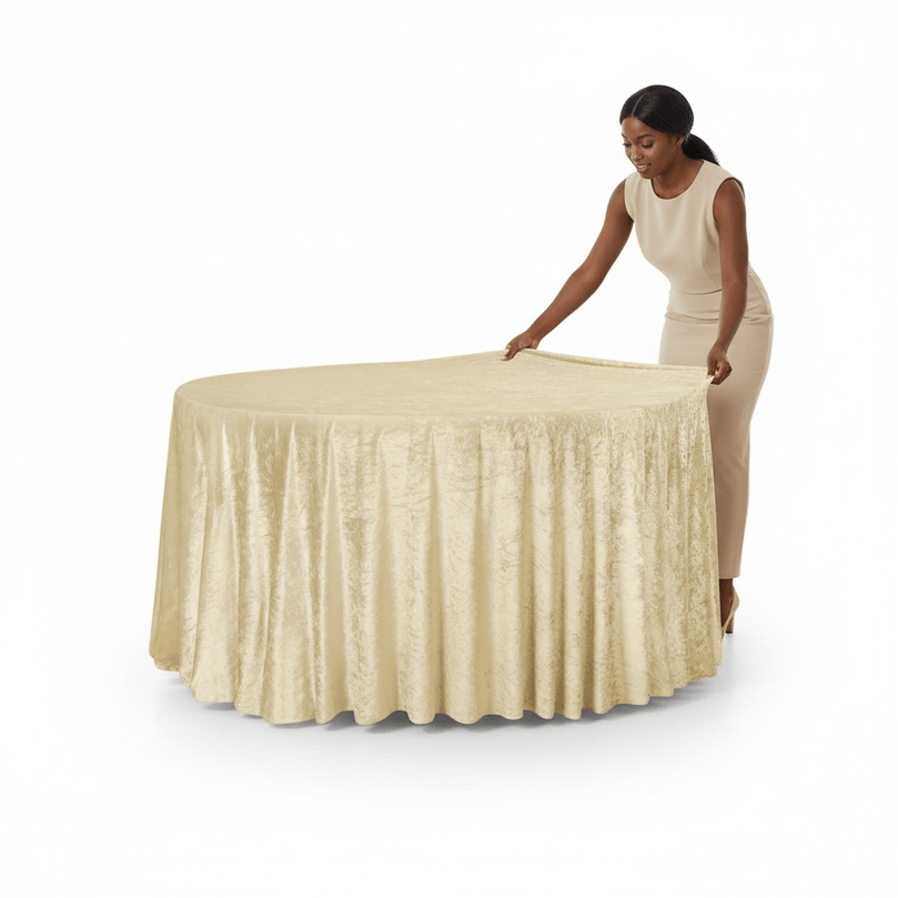 Woman in a beige dress setting up a round table with a champagne velvet tablecloth on a white background