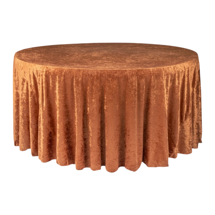 Round table covered with a rustic terracotta velvet tablecloth on a white background