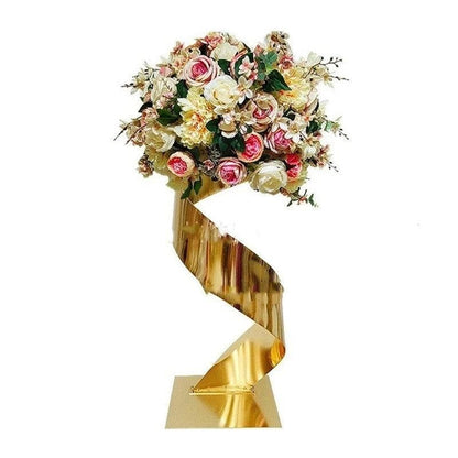 A spiral gold-finished metal flower stand with a lush arrangement of pink and yellow roses and various other flowers, designed as a wedding dining centerpiece.