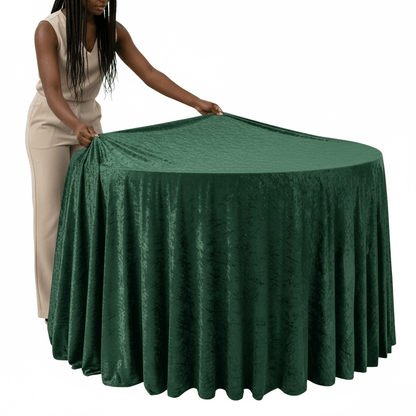 Person adjusting an emerald green velvet tablecloth on a round table