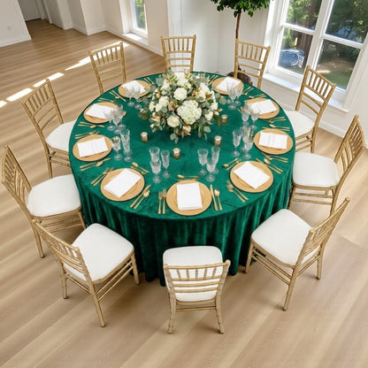 Round table set for a wedding event with emerald green tablecloth, gold plates, and chairs.
