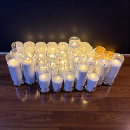 Multiple white candles in glass holders arranged on a wooden surface with a dark background.
