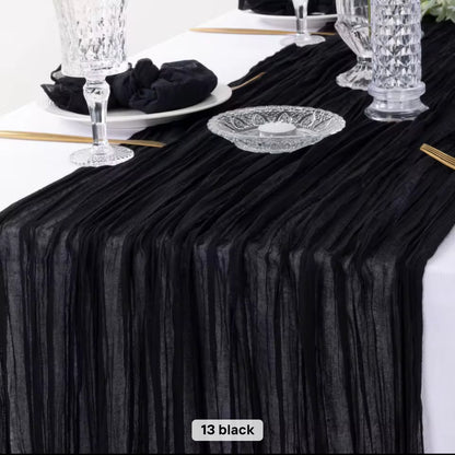 Black cheesecloth table runner on a white table with decorative items.