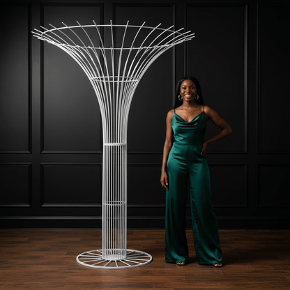 Woman in a green jumpsuit standing next to a modern white party rental sculpture against a dark paneled wall.