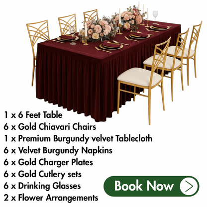 Table setting with burgundy velvet tablecloth, gold chairs, and floral arrangements on a white background.