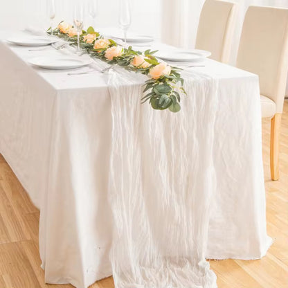 Table setting with a floral runner on a white cheesecloth table runner in a bright room.