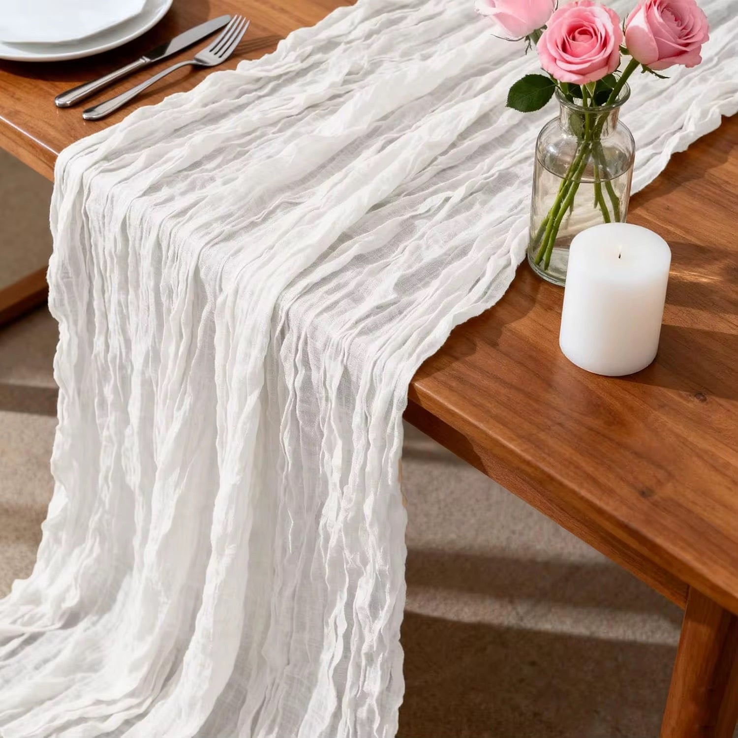 White cheesecloth table runner on a wooden table with a candle and flowers.