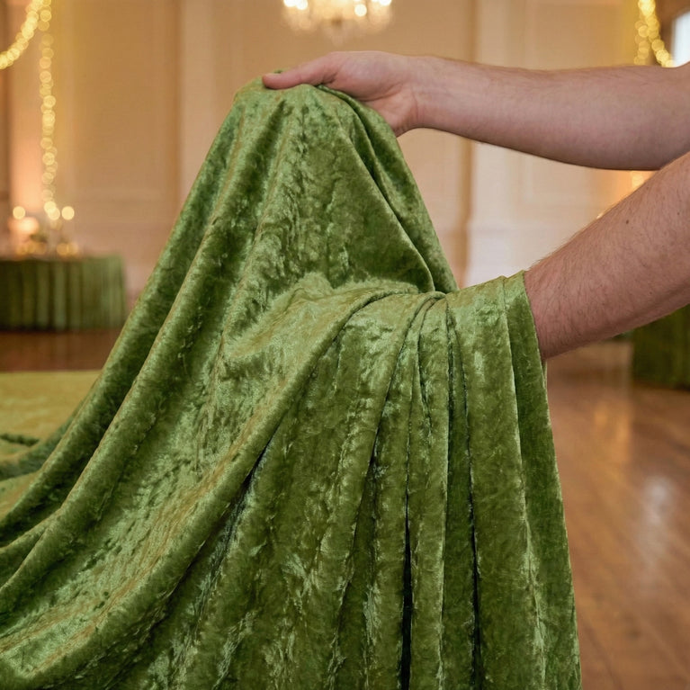 Person holding a sage green velvet tablecloth in an indoor setting with blurred background