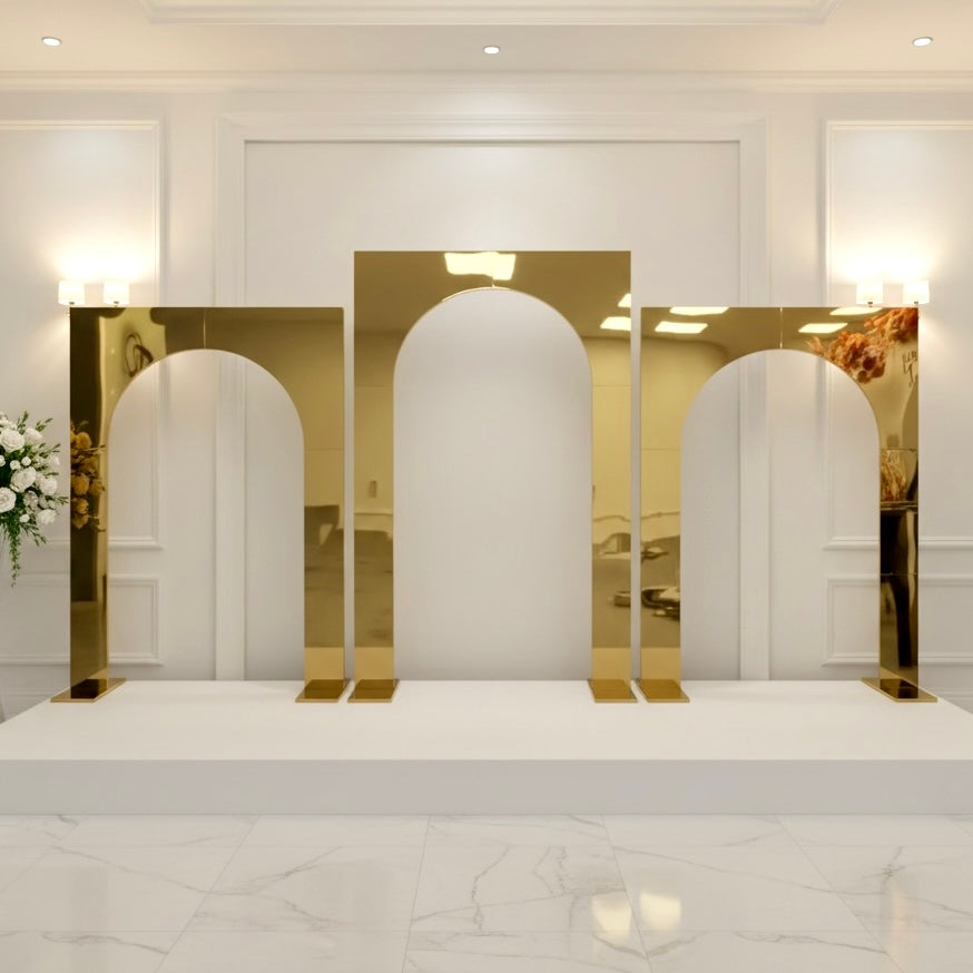 Gold arch-shaped mirror wedding backdrops on a white platform with a white wall and lights in the background