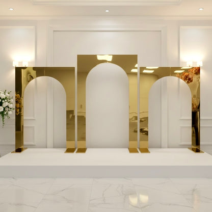 Gold arch-shaped mirror wedding backdrops on a white platform with a white wall and lights in the background